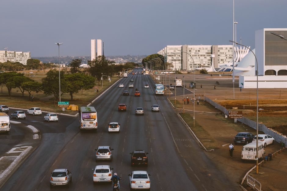Ações do GDF — Aerial view of Brasília's urban traffic with prominent government buildings and a bustling road.